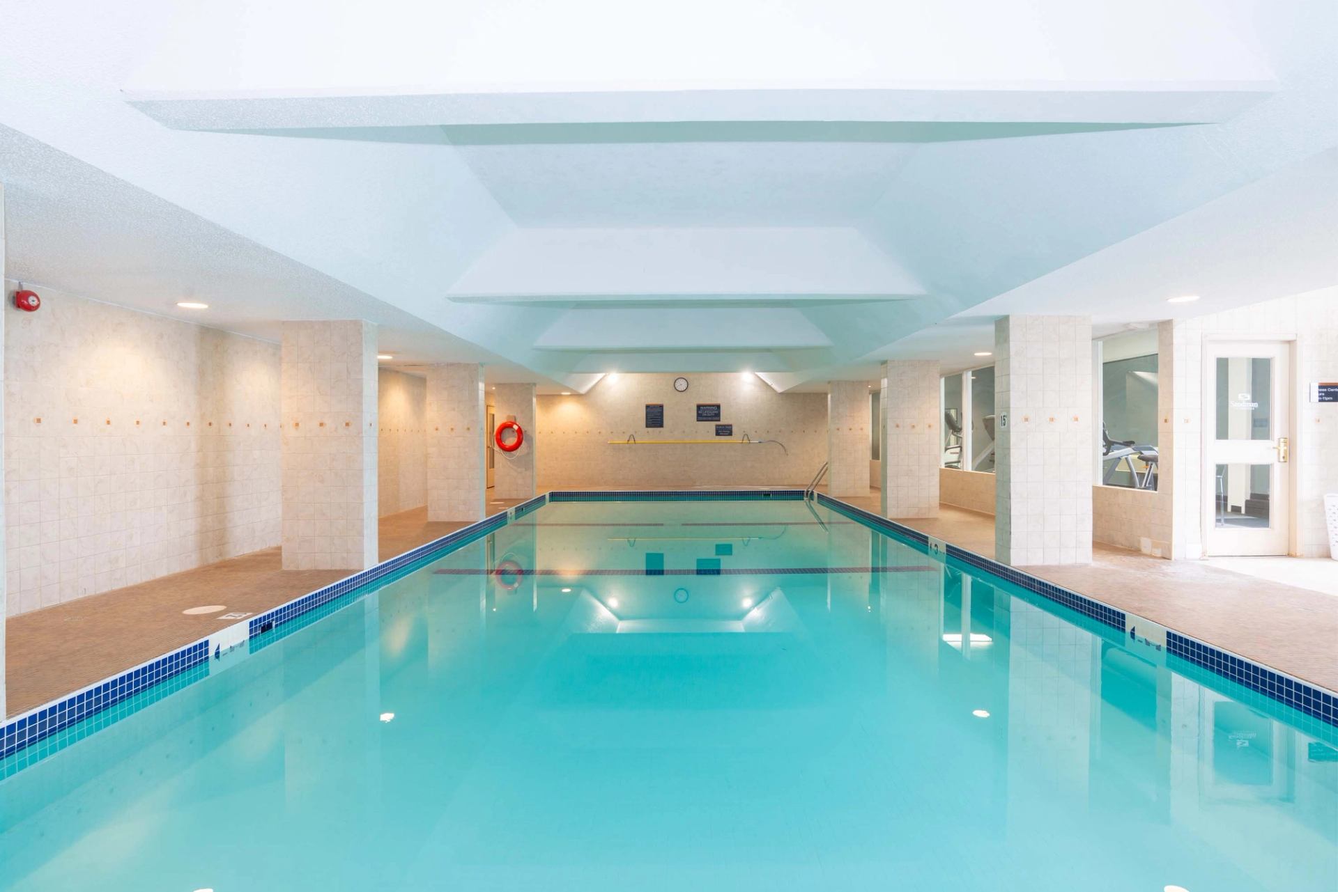 An indoor hotel swimming pool with clear water and tiled deck area.