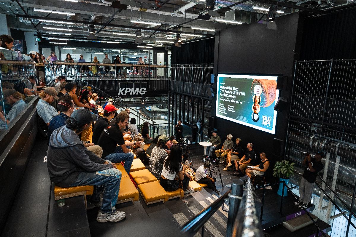 Audience watches a panel on diversity and inclusion at an indoor event with a large screen.