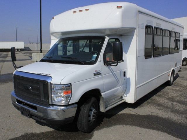 White CST Transportations bus with large windows parked on paved surface.
