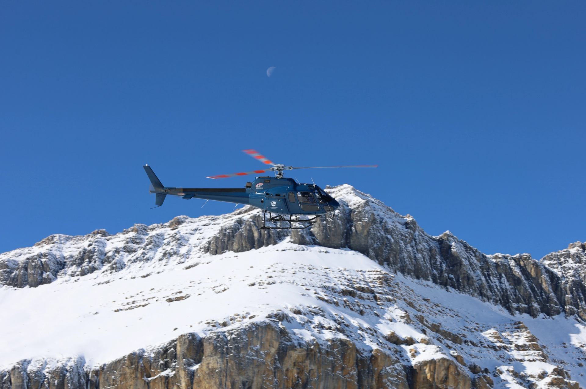 Helicopter flying above snow covered mountain peaks in the Canadian Rockies.