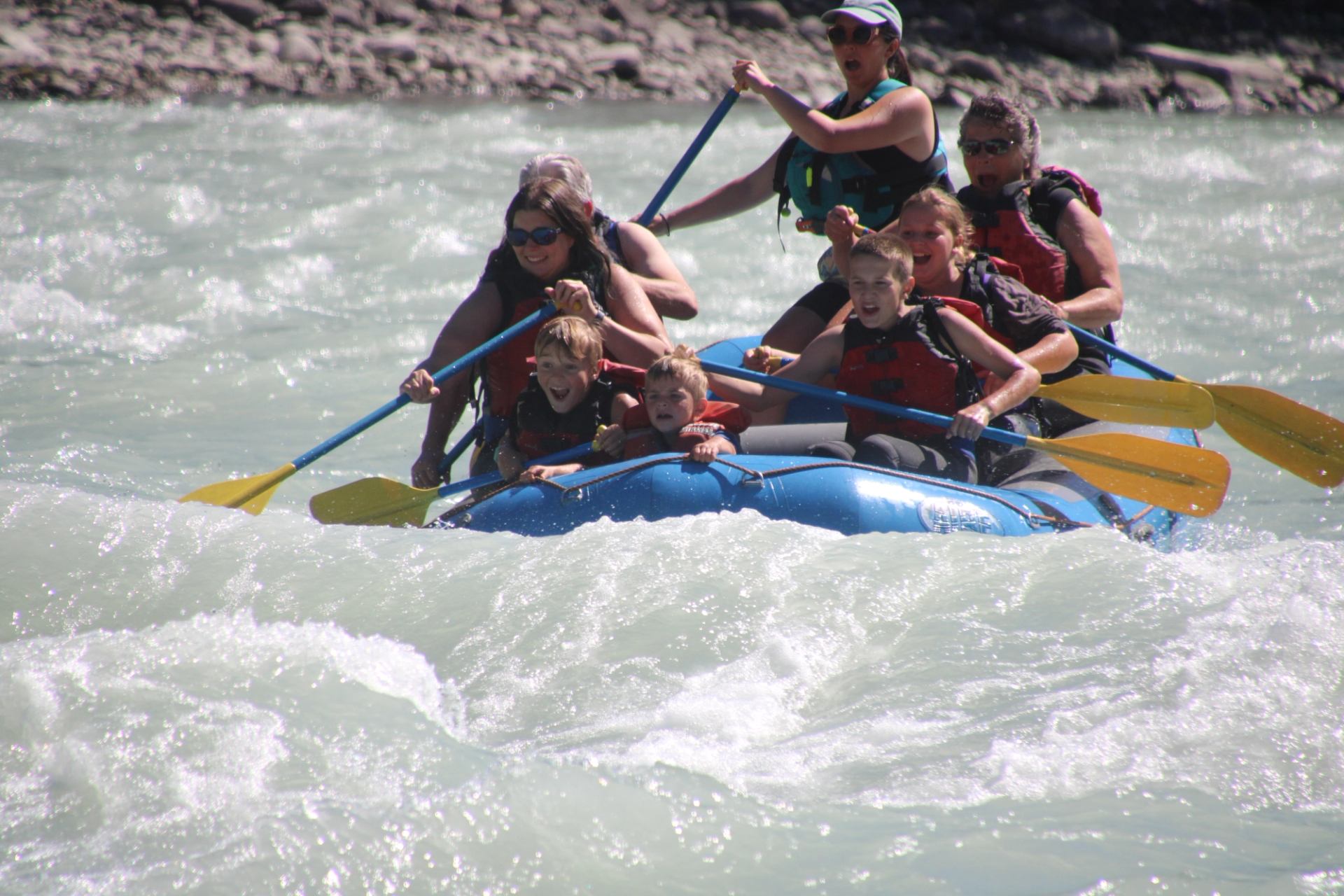 Rafting group charging through swift whitewater on a bright, fast-moving river.