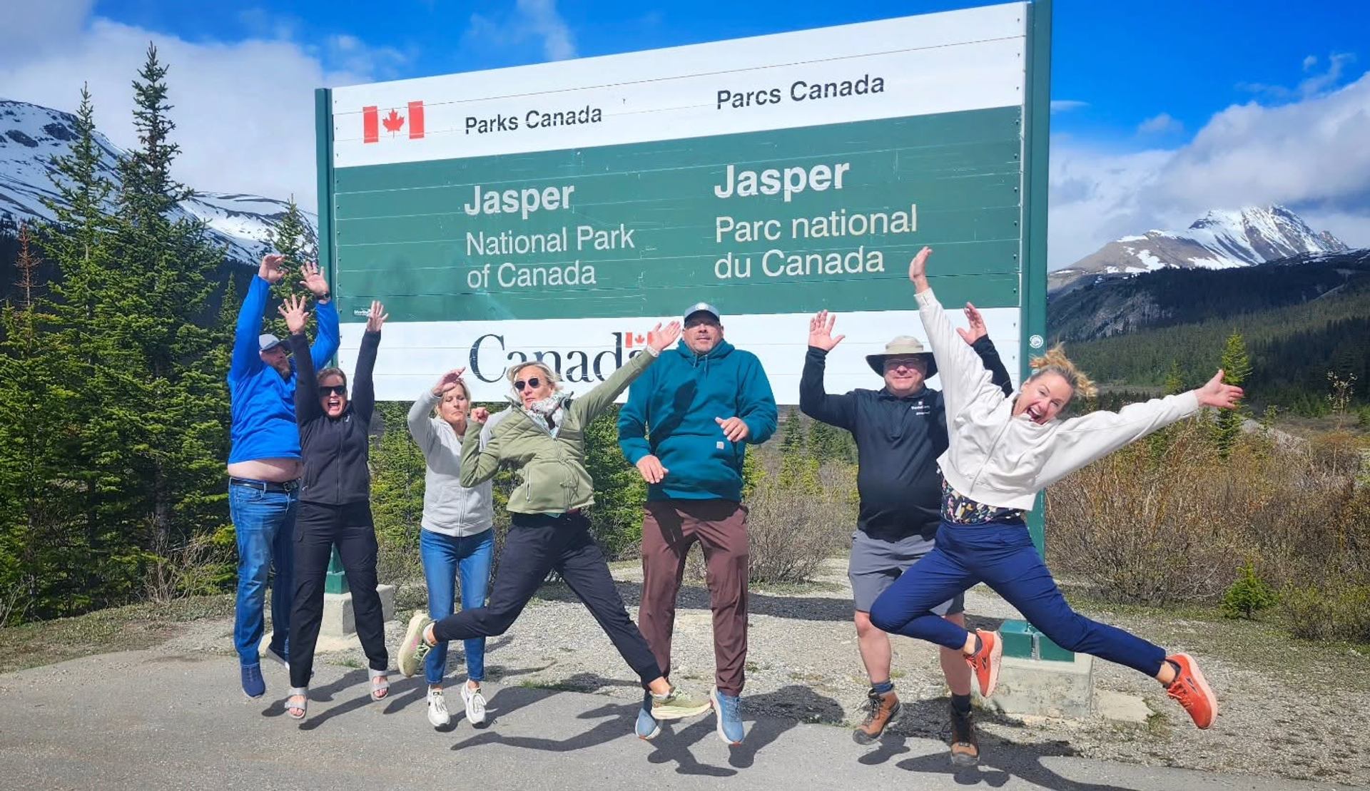 Group of people jumping in front of Jasper National Park of Canada entrance sign.