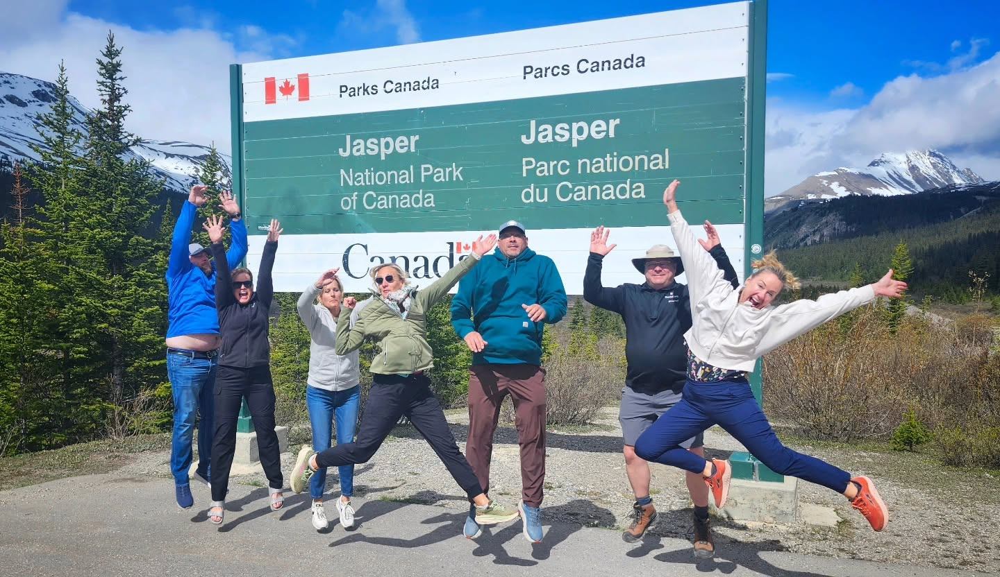 Group of people jumping in front of Jasper National Park of Canada entrance sign.