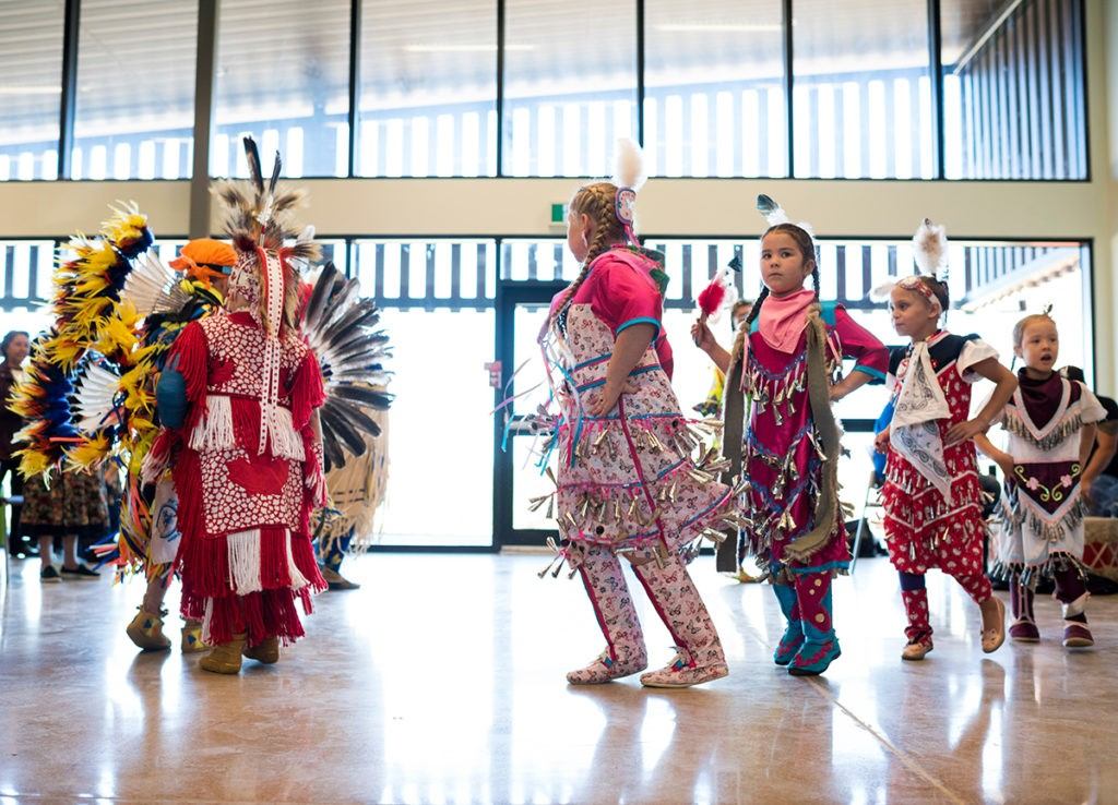 Children in traditional dance outfits perform inside Fort McKay Youth Centre gymnasium.