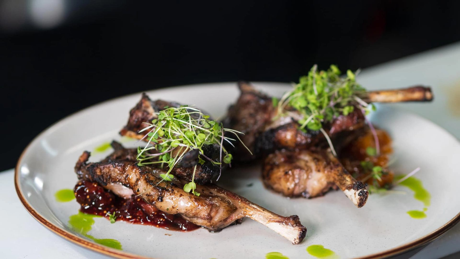 Grilled meat chops with microgreens and dark sauce on a white plate.