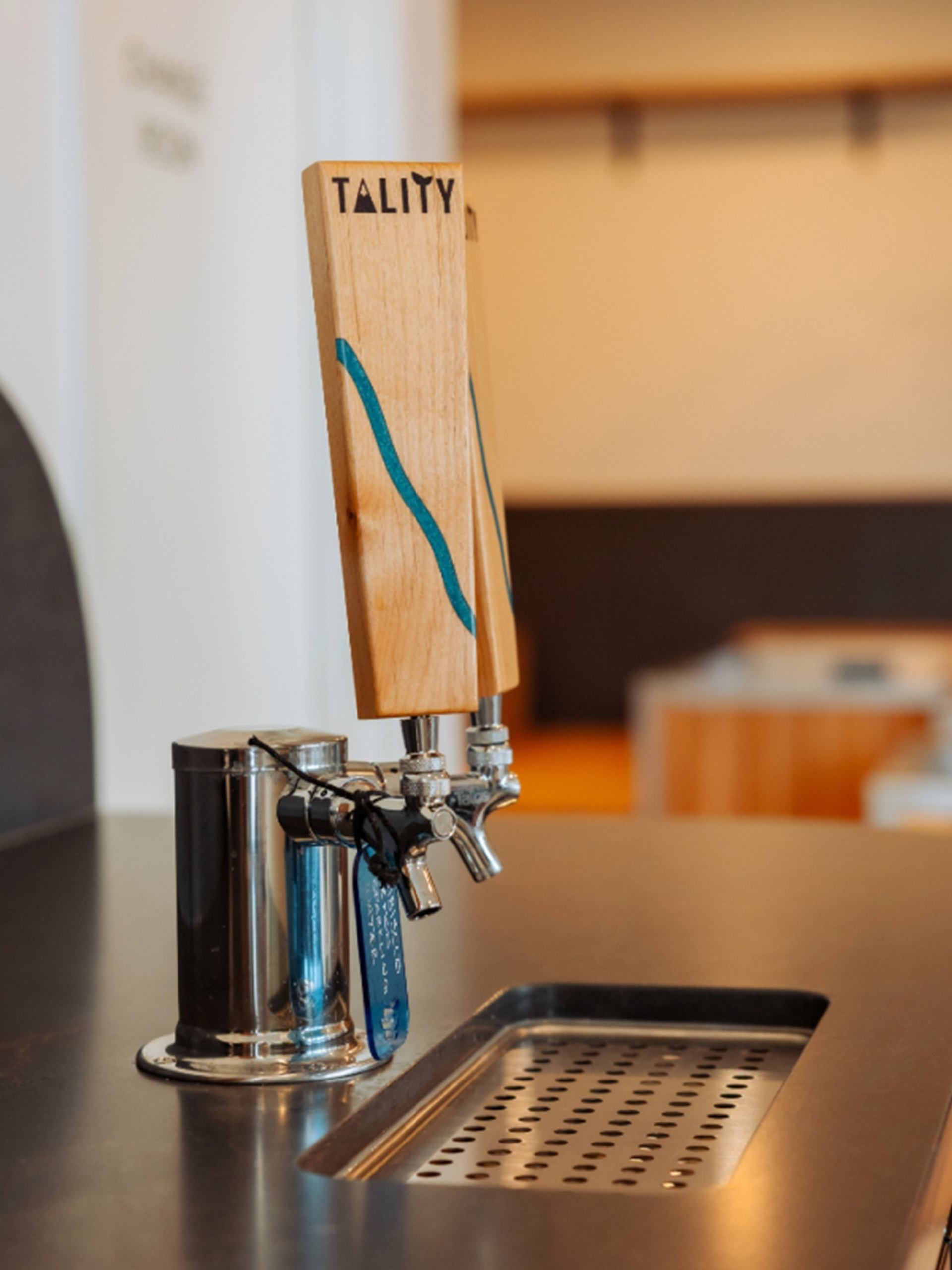 Draft beer taps with wooden TALITY handles on a stainless steel bar counter.