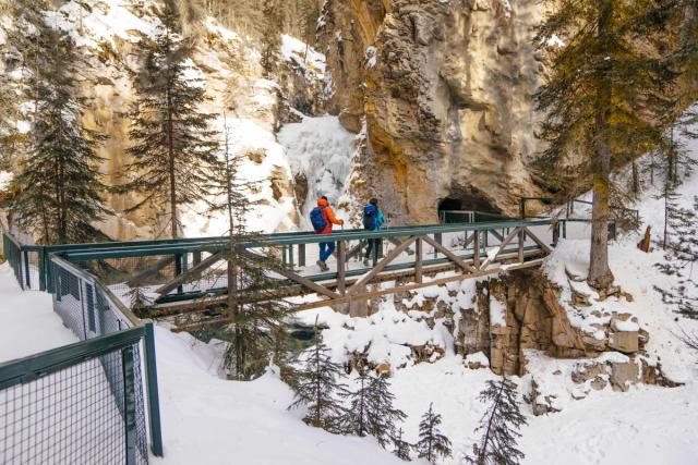 A couple winter hiking over a bridge  heading toward a cave opening to the lower falls at Johnston Canyon.