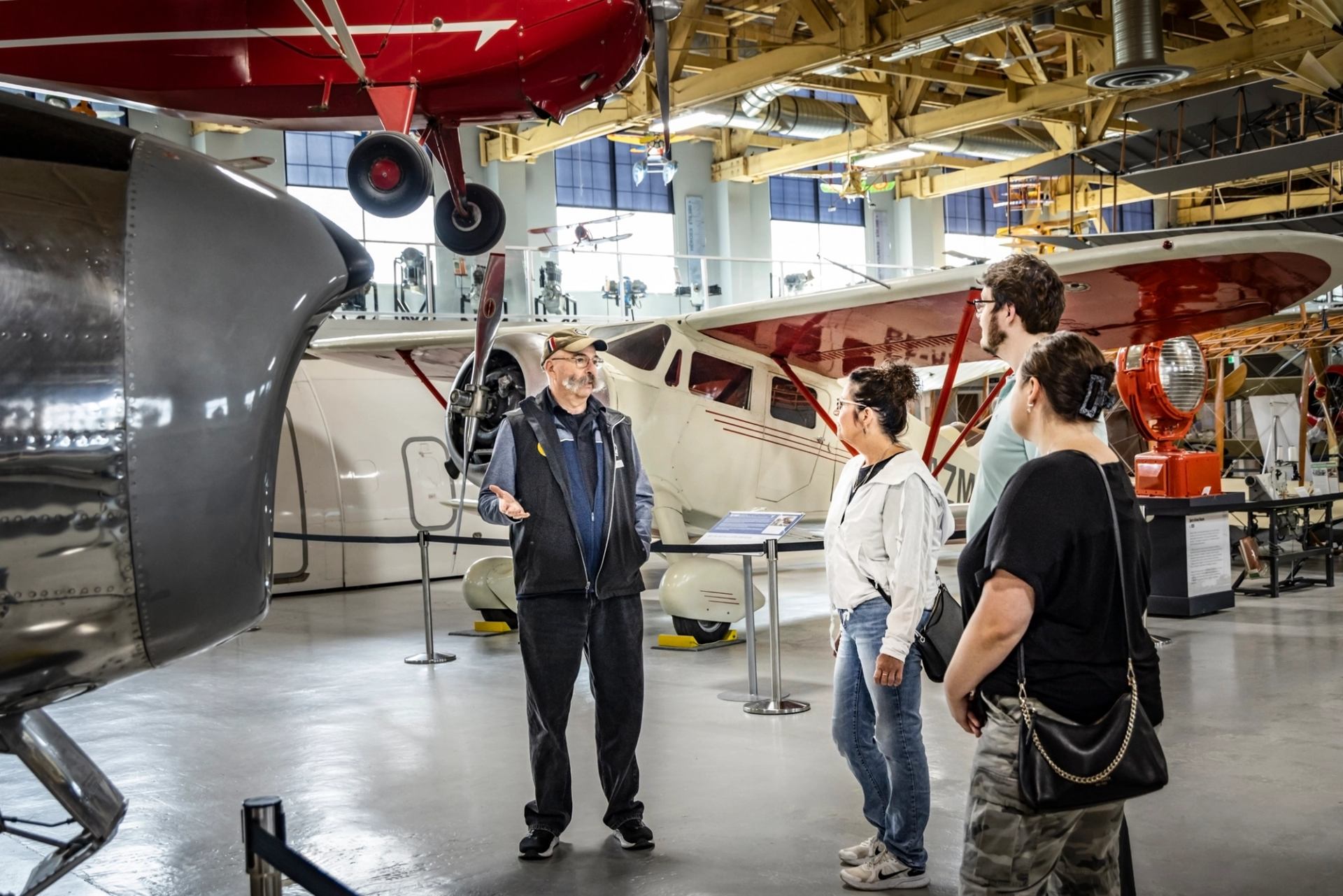 Aircraft hangar exhibit with visitors standing beside a parked propeller airplane and engine.