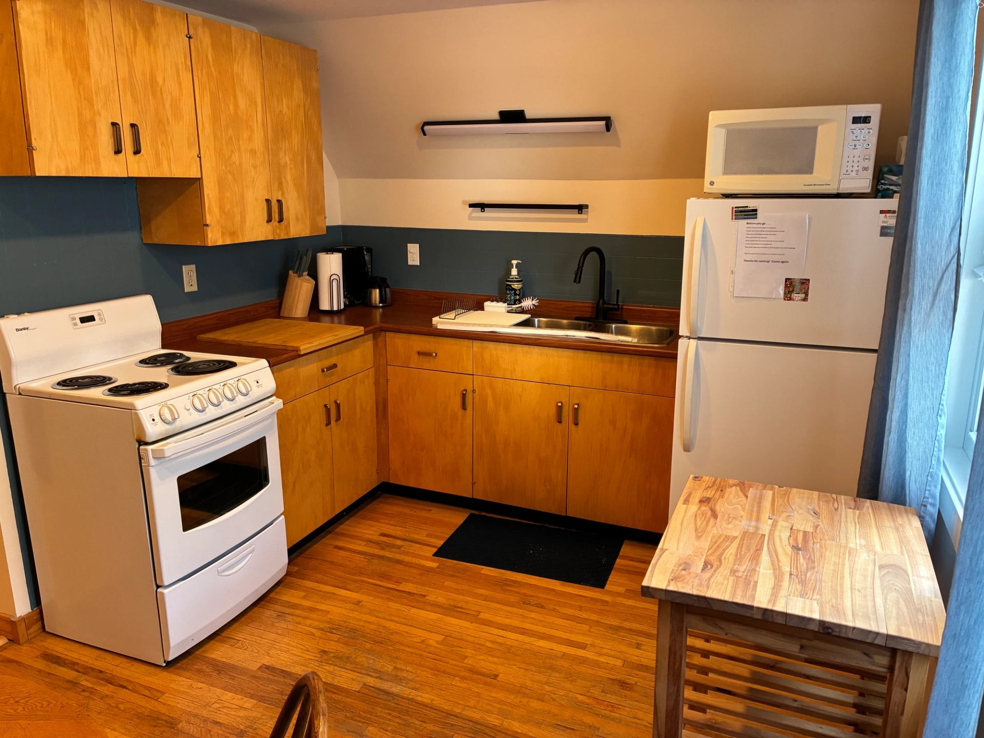 Small kitchen with wood cabinets, white stove, fridge, microwave and countertop appliances.