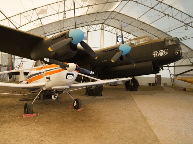 Large black warplane and smaller aircraft inside tented area