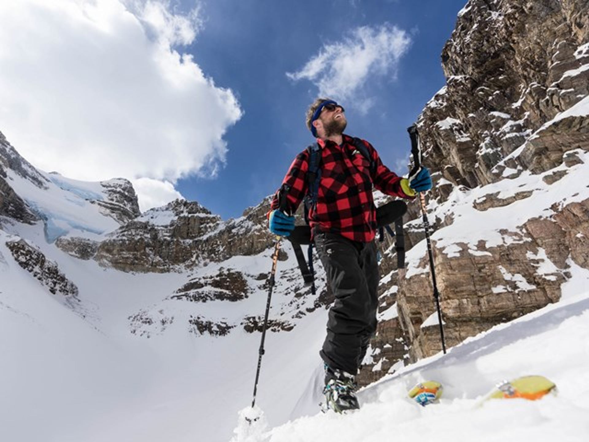 Mountaineer standing on snowy terrain with poles, surrounded by steep rock and glacier-covered peaks.