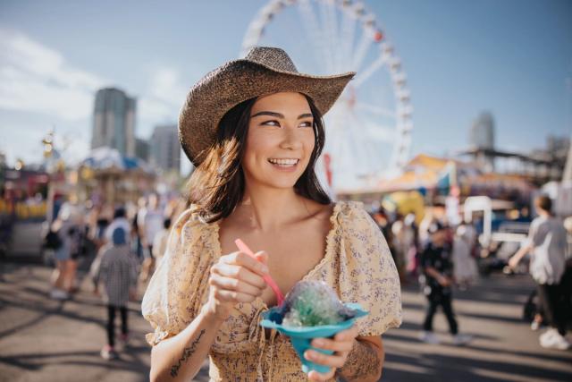 Women eating a snow cone with the Calgary Stampede midway in the background.