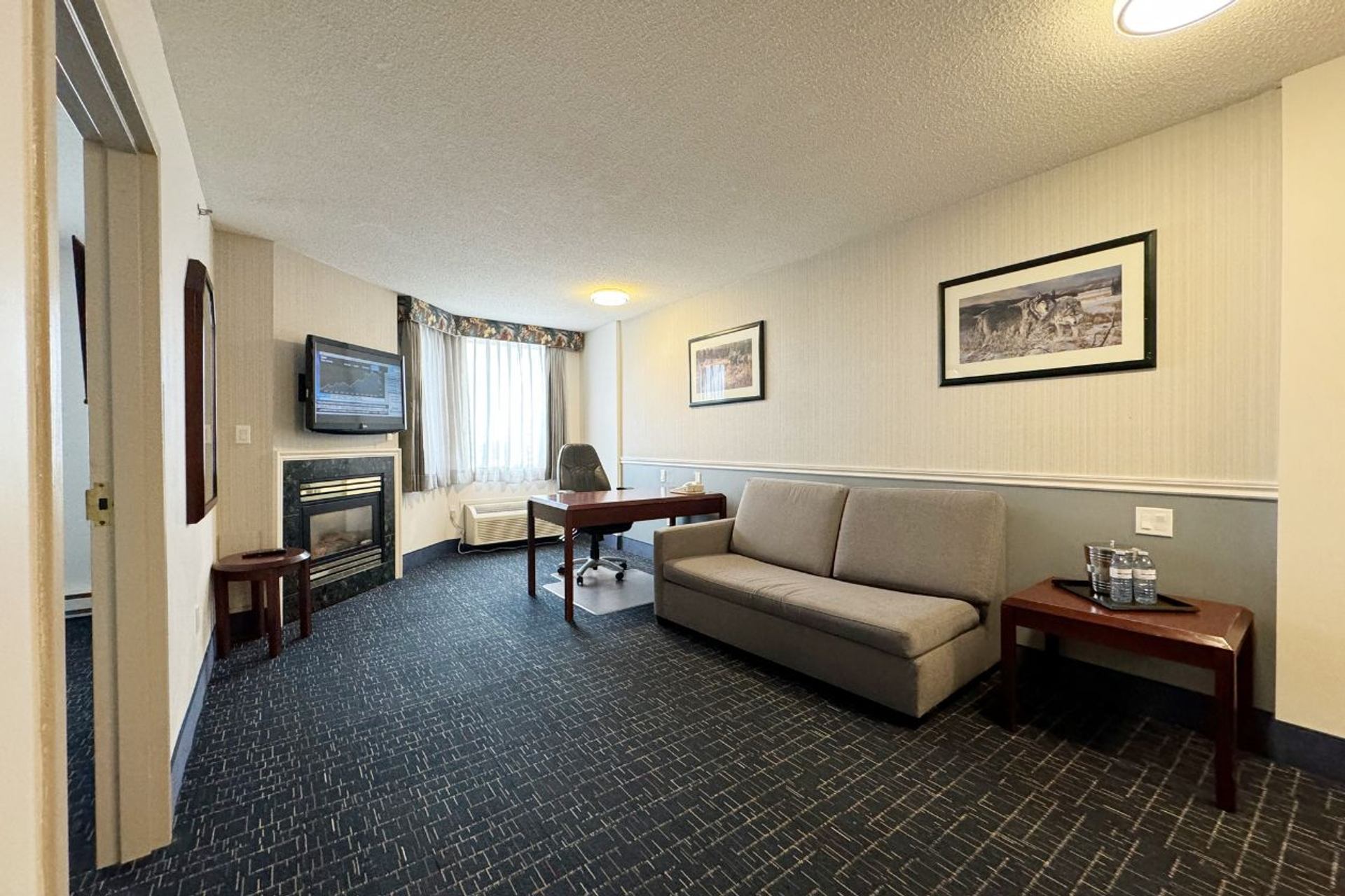 A suite living area includes a sofa, fireplace, work desk, television, and large sunlit window.