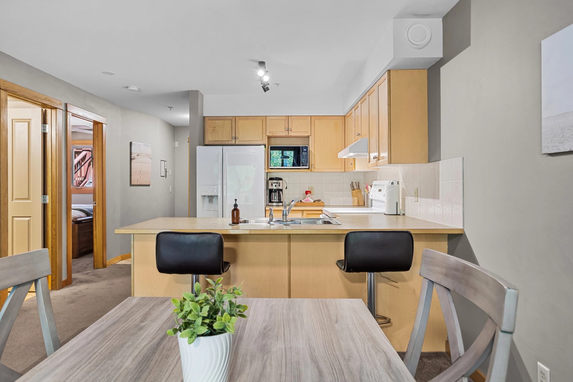 Kitchen with wood cabinets, breakfast bar, two stools, and dining table with plant centerpiece/