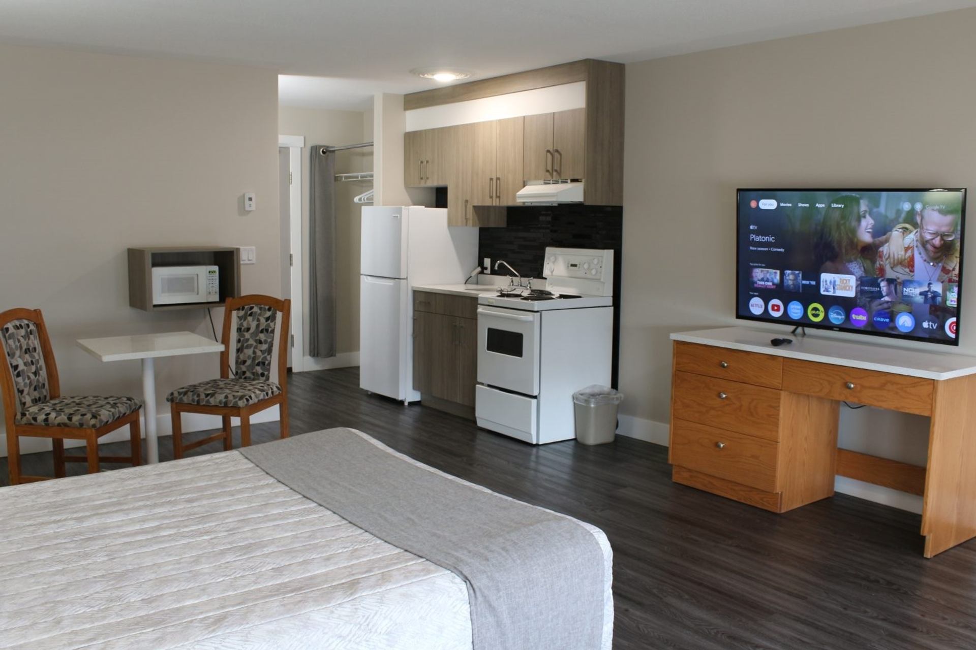 Spacious motel room with bed, dining set, kitchen appliances, and flat-screen TV.