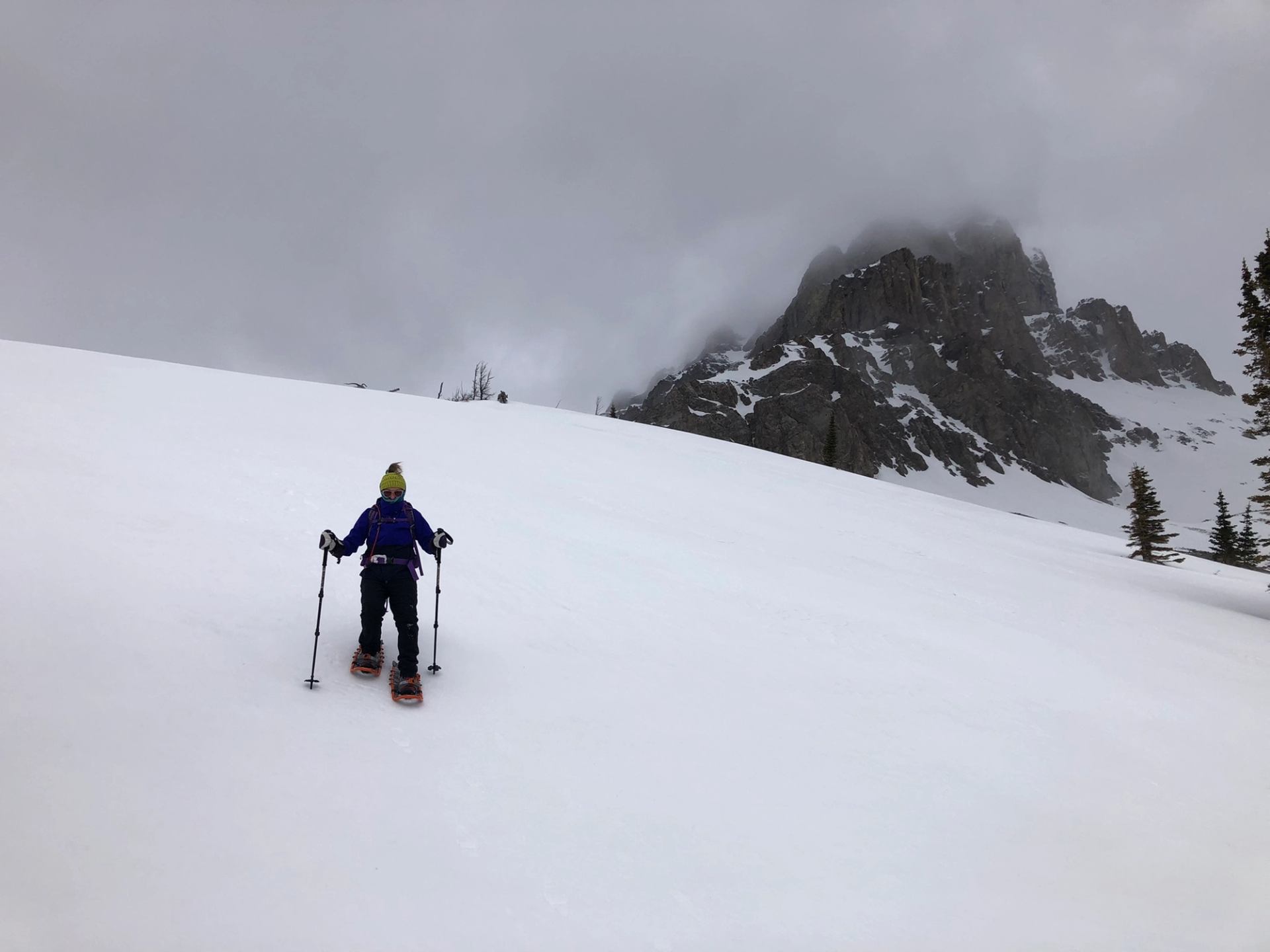 Snowshoer ascending a wide snowy slope with misty mountain peak in the background.