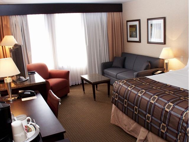 Hotel room with bed, seating chair, small table, and bedside lamps on both sides.