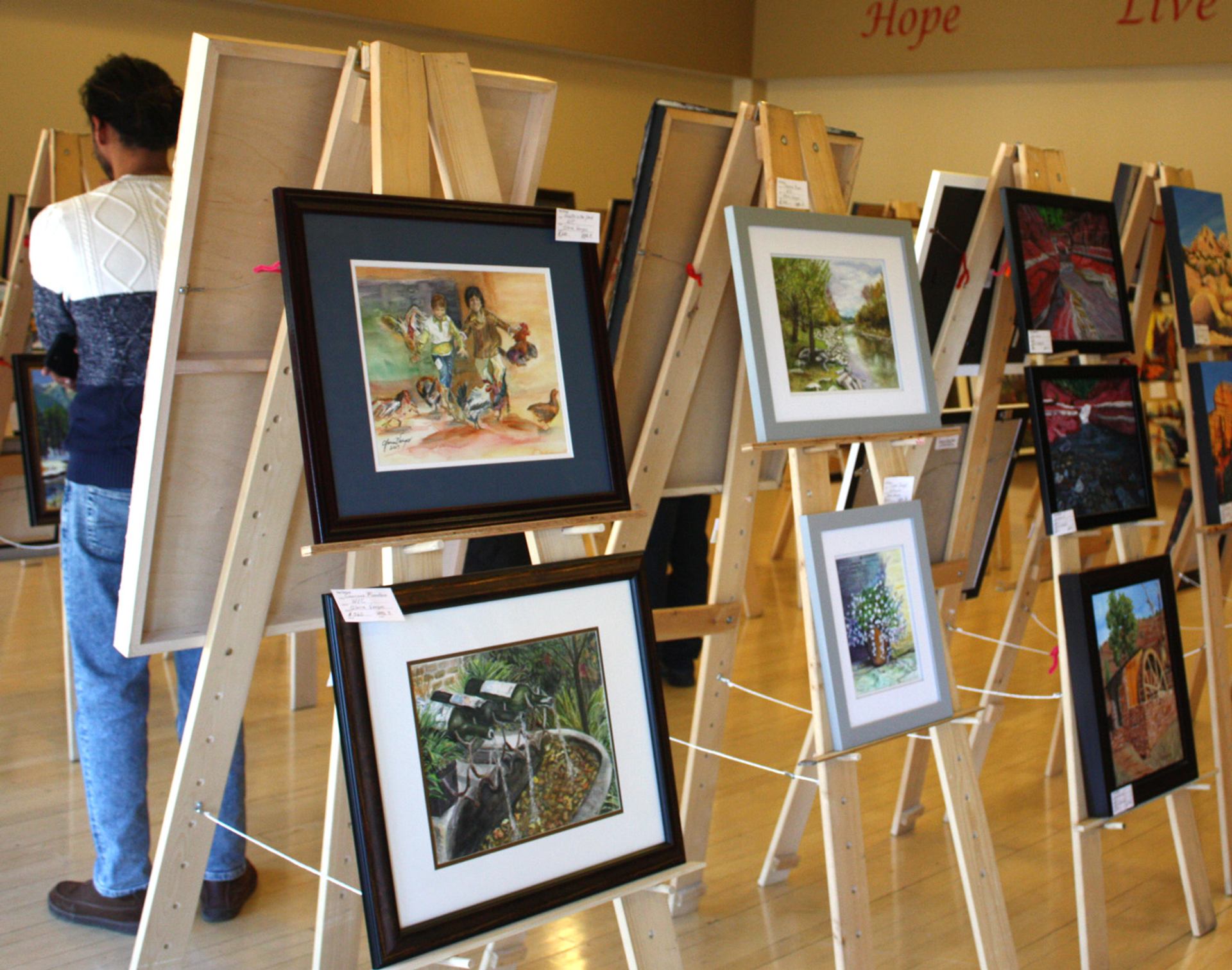 Framed paintings on wooden easels in a gallery, with a person viewing artwork.