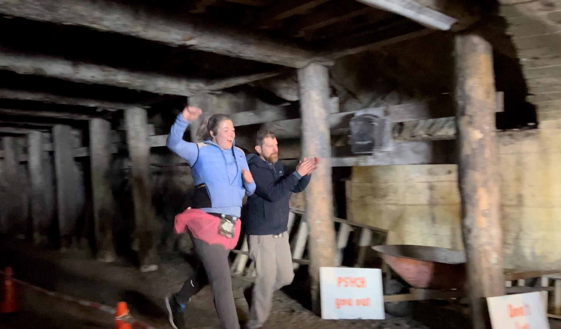 Two participants celebrate while running through a wooden-supported tunnel.