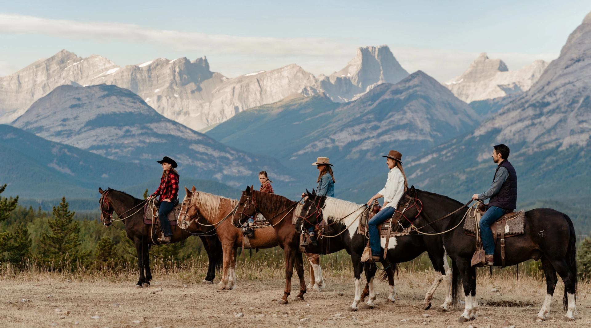 A group of riders in front of towering mountains and a forest.