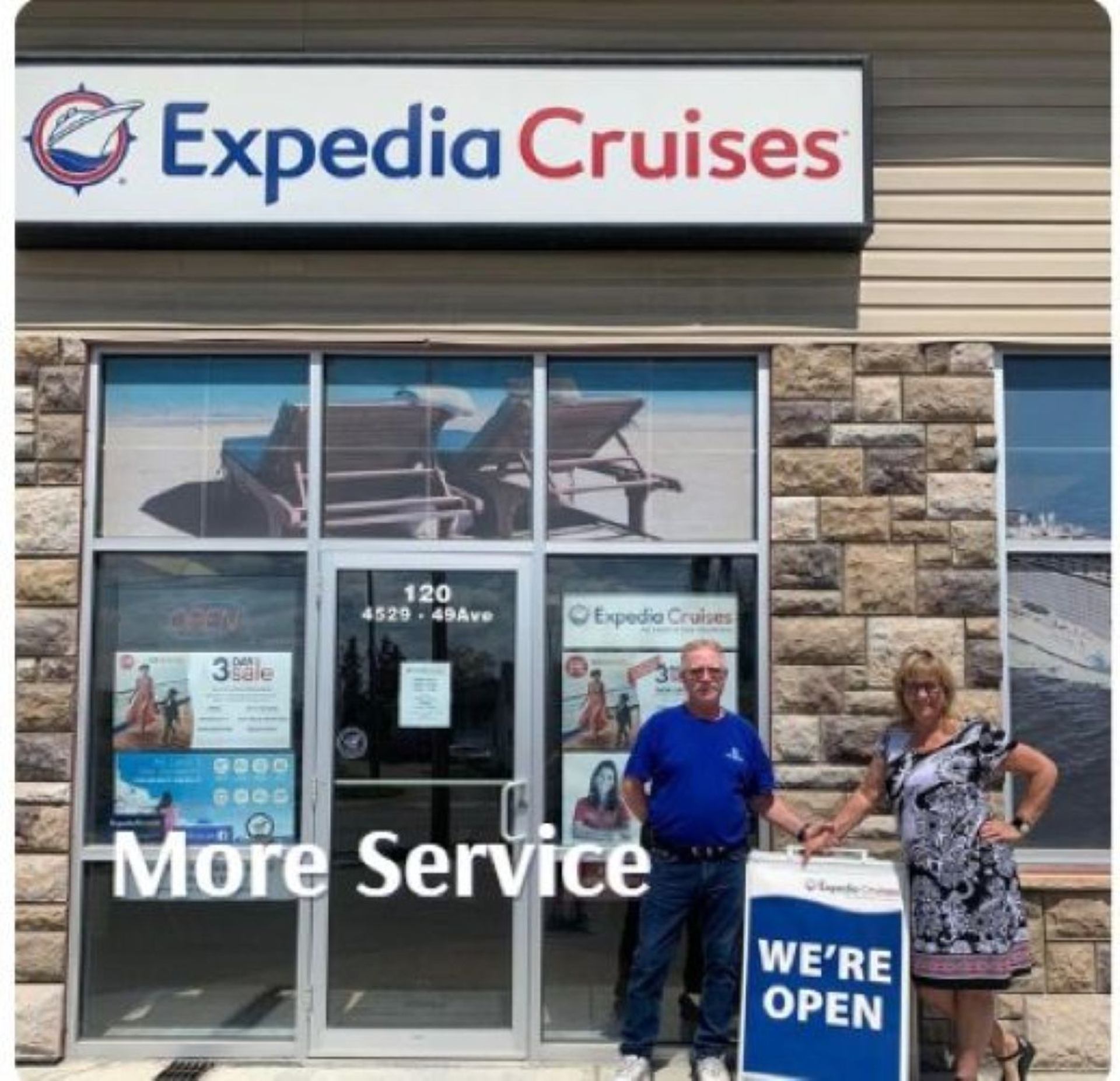 Two people stand outside Expedia Cruises beside a sign reading “We're open.”