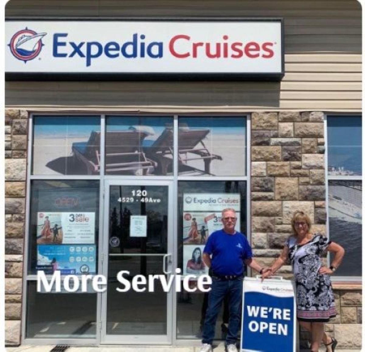 Two people stand outside Expedia Cruises beside a sign reading “We're open.”