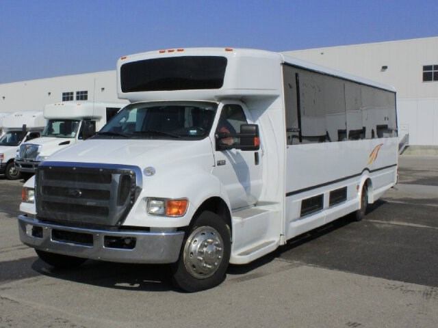 Large white CST Transportations bus with tinted windows parked near industrial building.