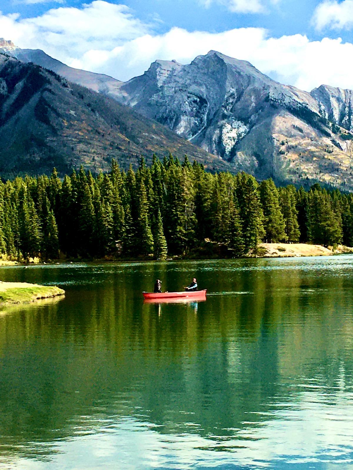 Two people in a boat in the beautiful turquoise waters with the Rockies in the background