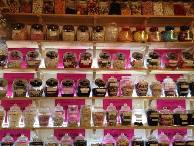 Jars of candy and ice cream toppings displayed on shelves inside a shop.