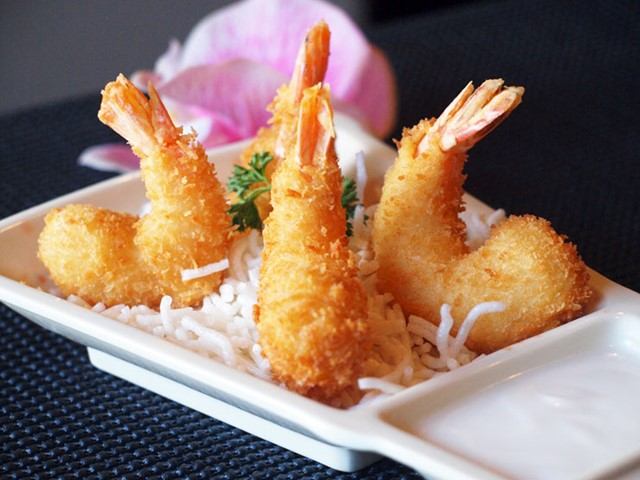Plate of fried shrimp with rice and herbs on a white square dish.