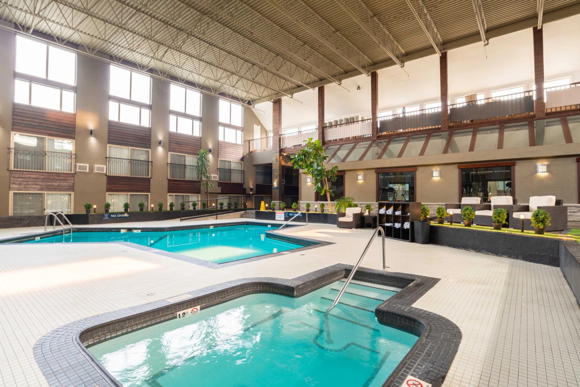 Indoor pool and hot tub set inside a spacious atrium with seating.