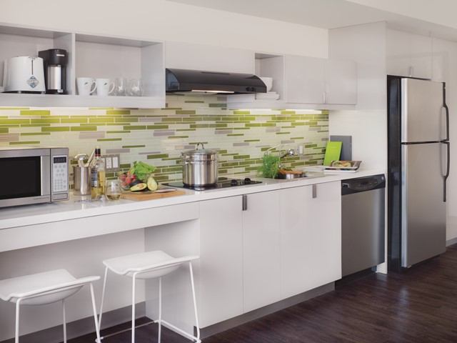 Modern hotel kitchen with white cabinets, mosaic backsplash, and bar stools.