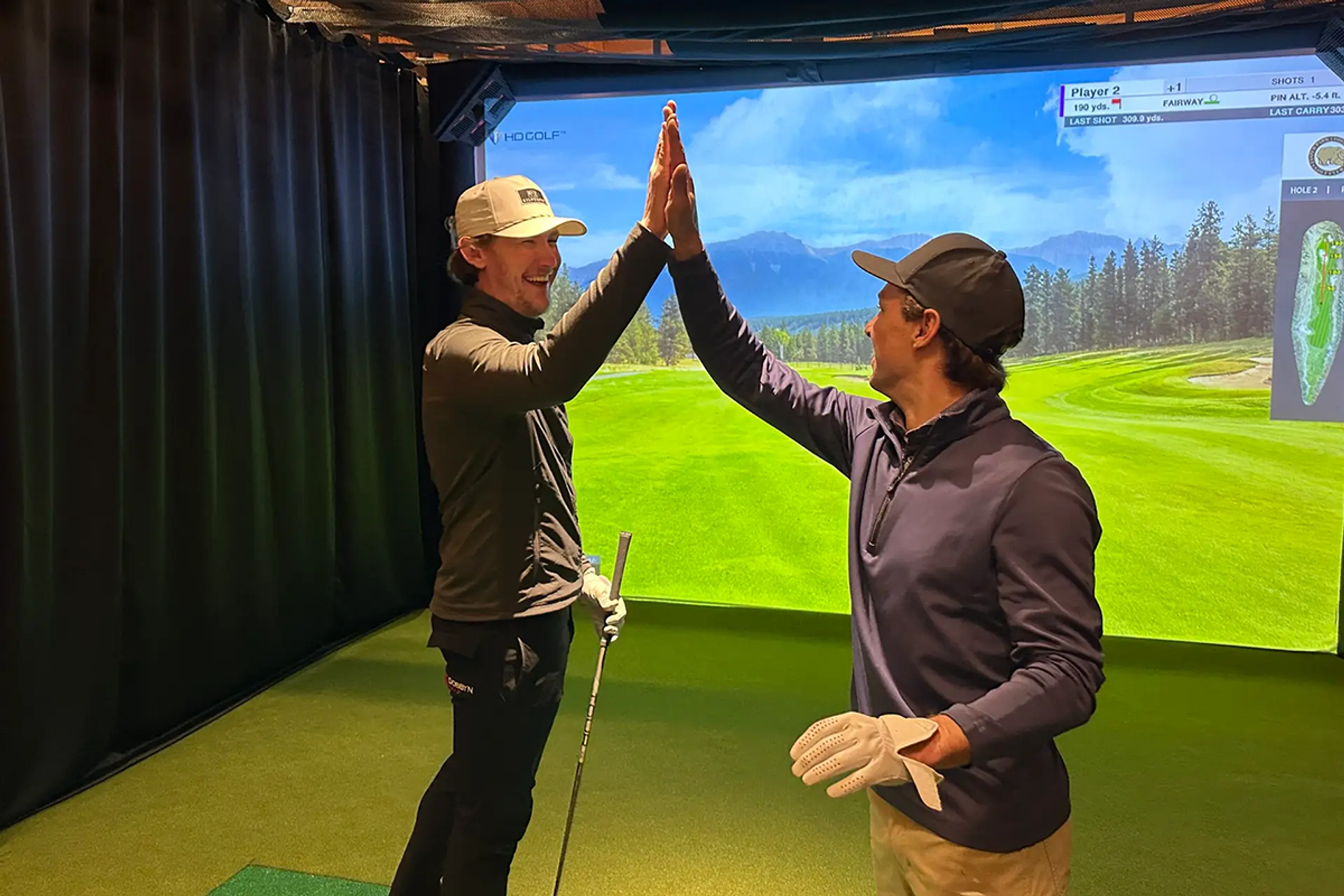 Two golfers giving a high-five in front of a golf simulator screen.
