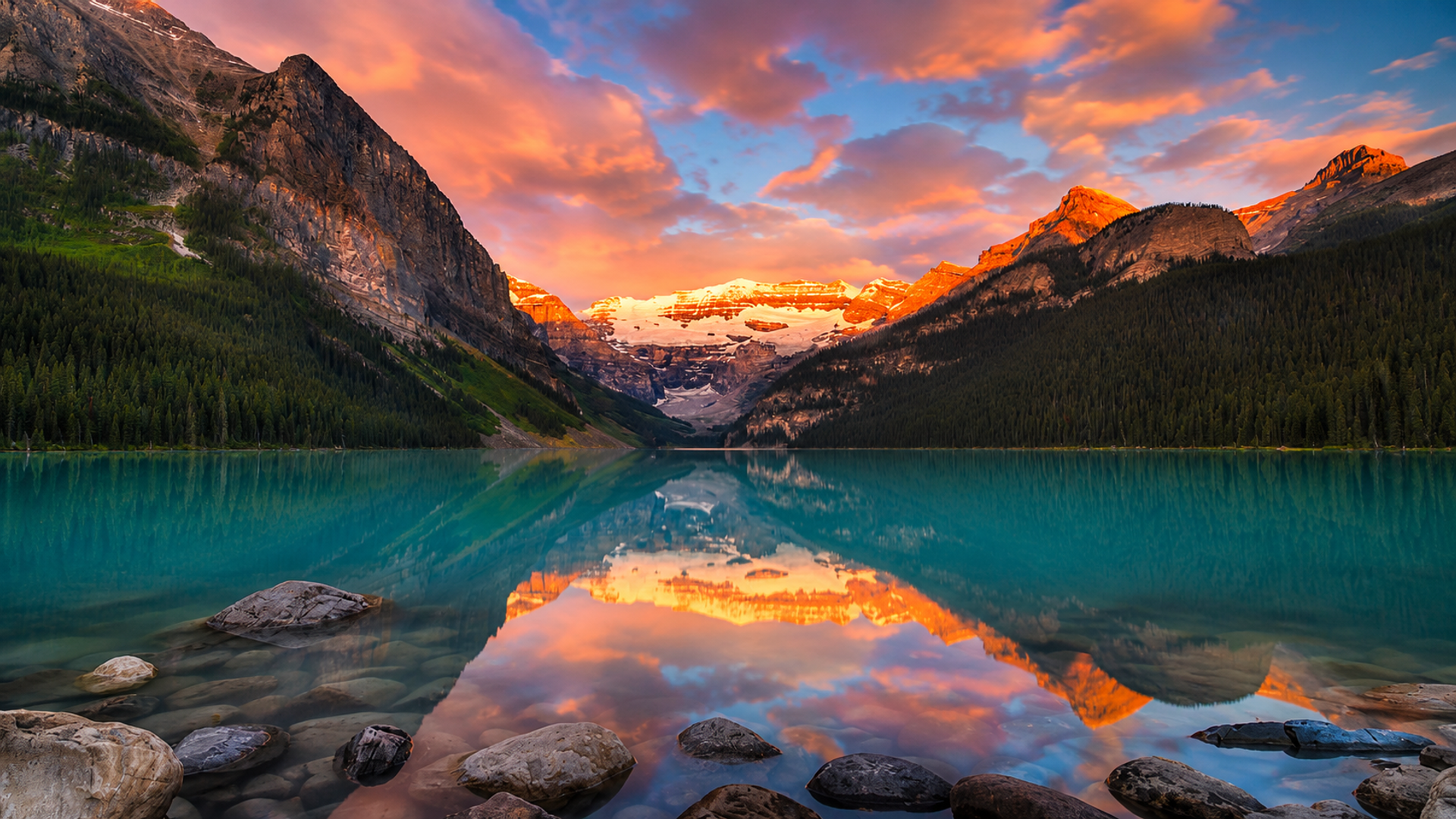 Turquoise lake reflects sunlit mountains, evergreen forests and pink clouds.