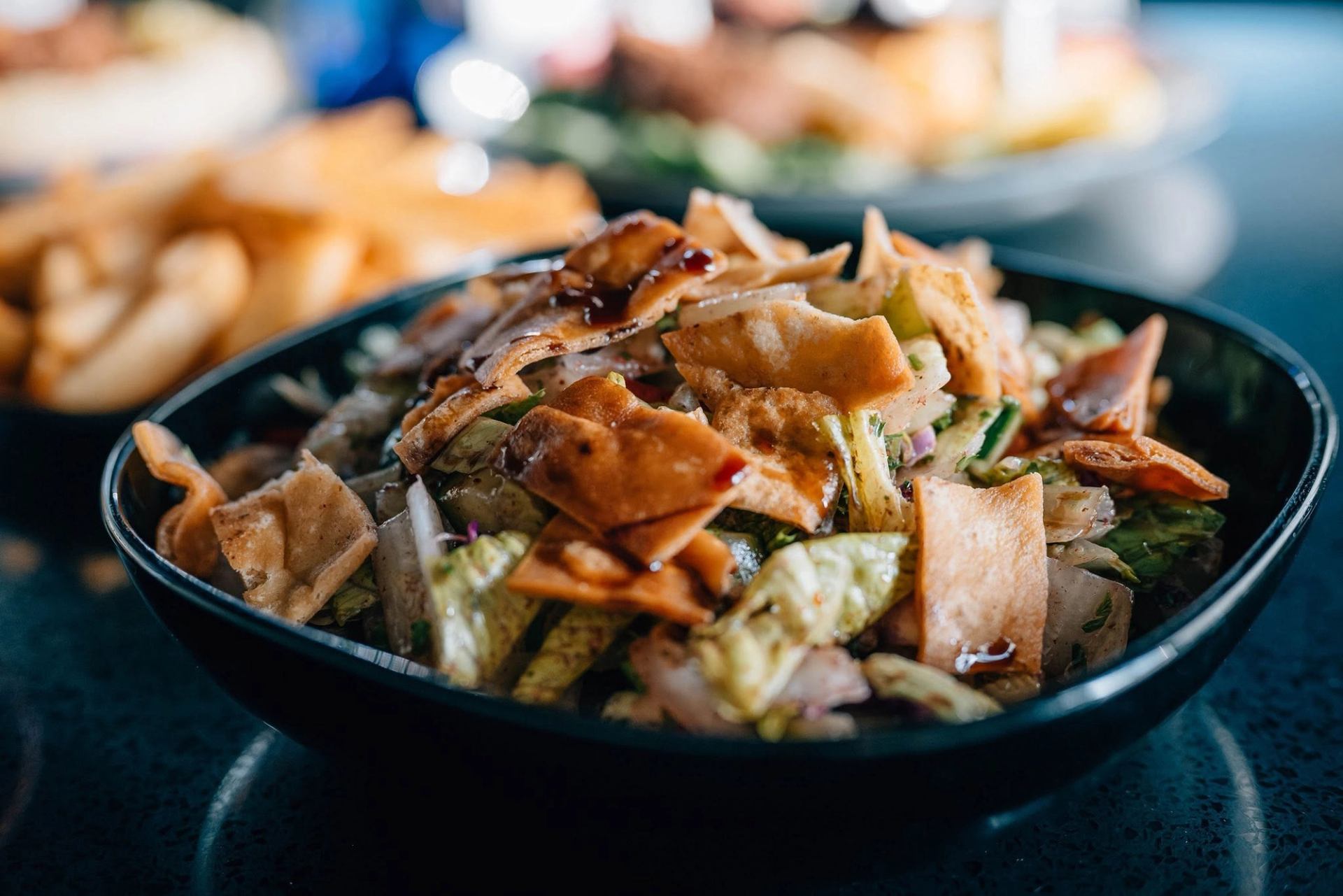 A fattoush-style salad is topped with crispy pita chips, fresh vegetables, and dressing.