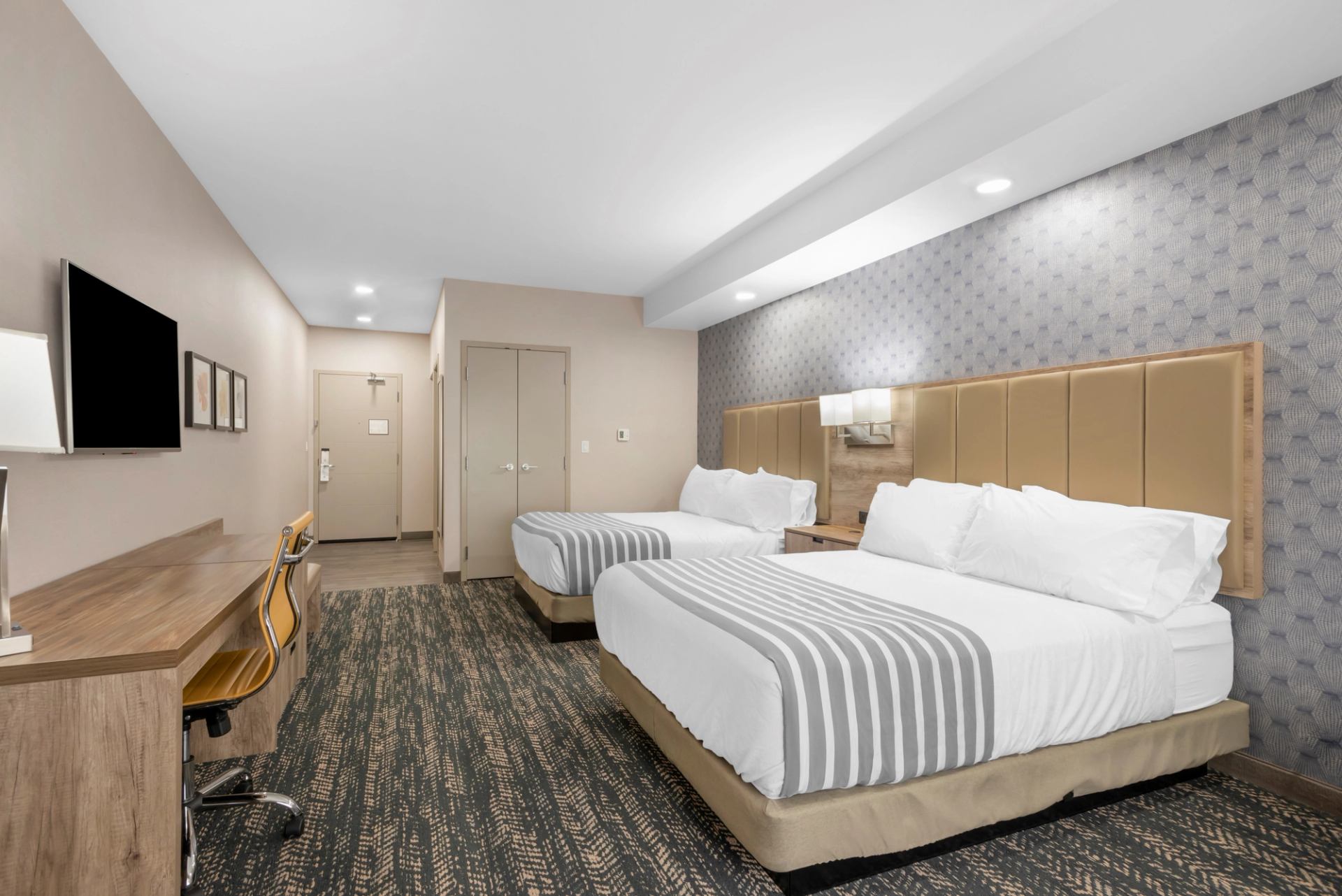 Modern hotel room with two beds, desk, and TV.