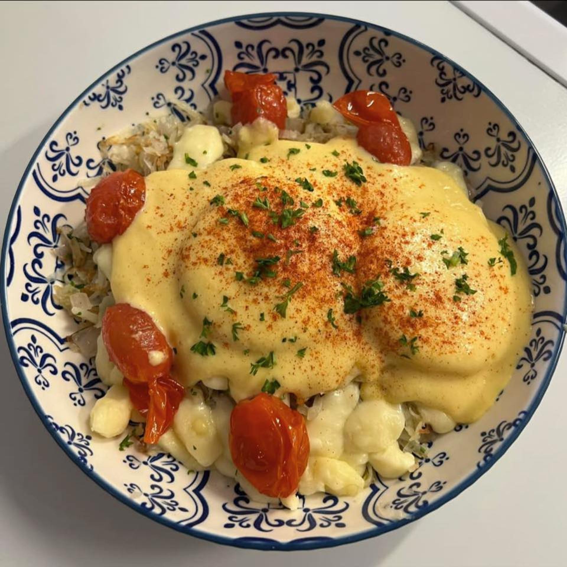 Bowl of eggs Benedict topped with hollandaise sauce and roasted cherry tomatoes