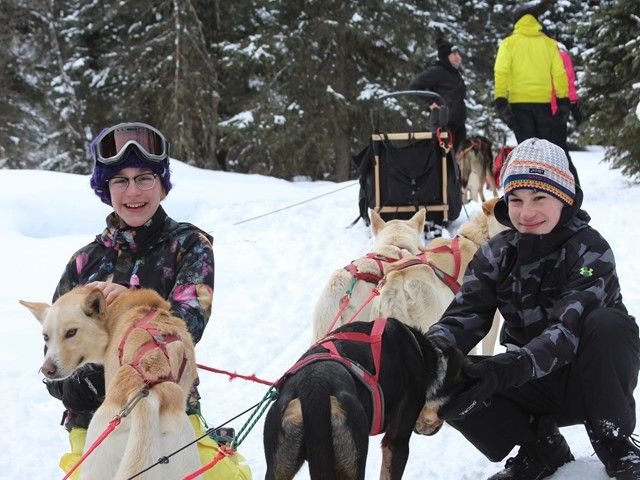 Two children pet sled dogs during an excursion.