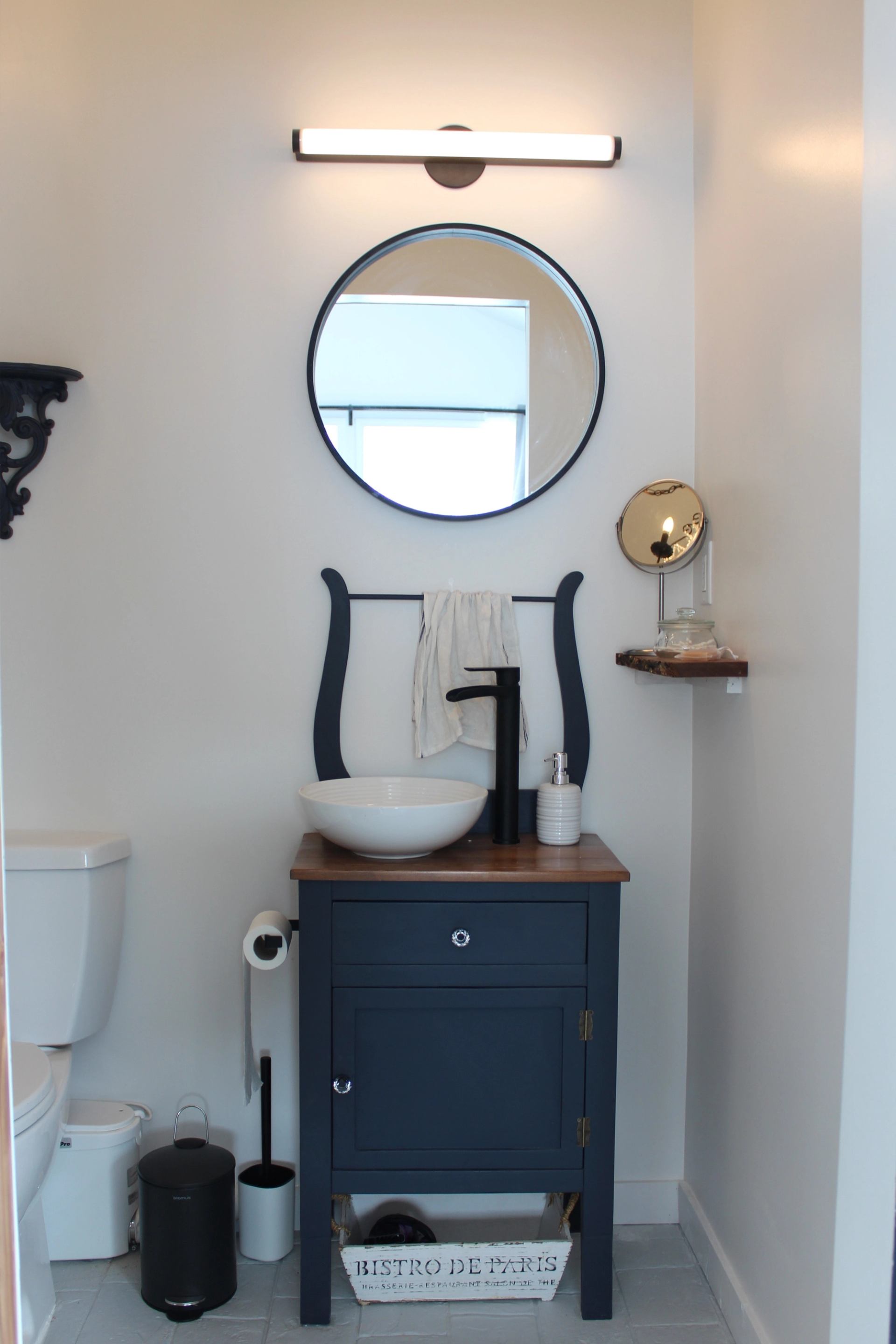 Bathroom vanity with vessel sink, round mirror, towel rack and toilet.