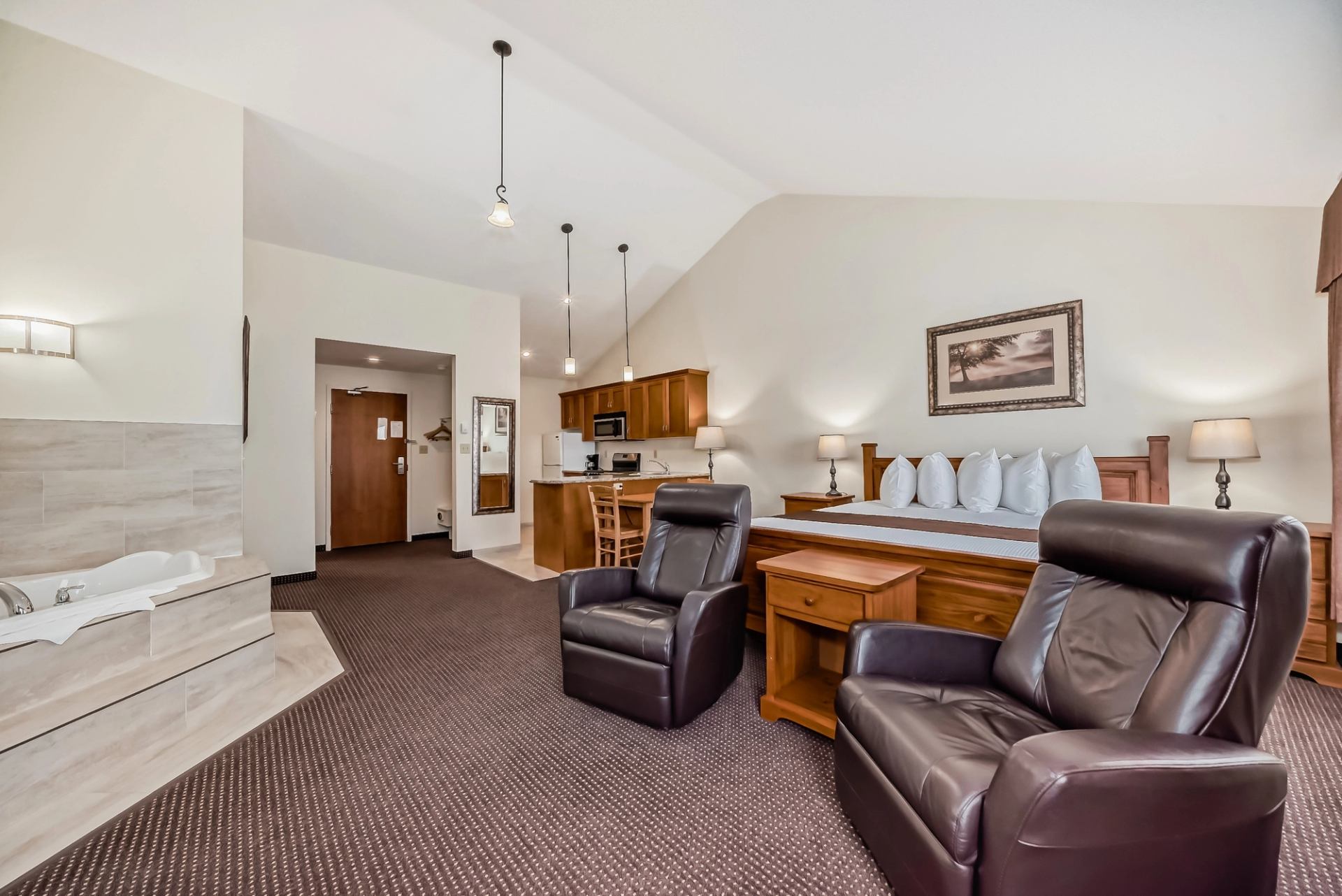 Hotel room featuring two leather recliners, a king bed, and a kitchenette in the back