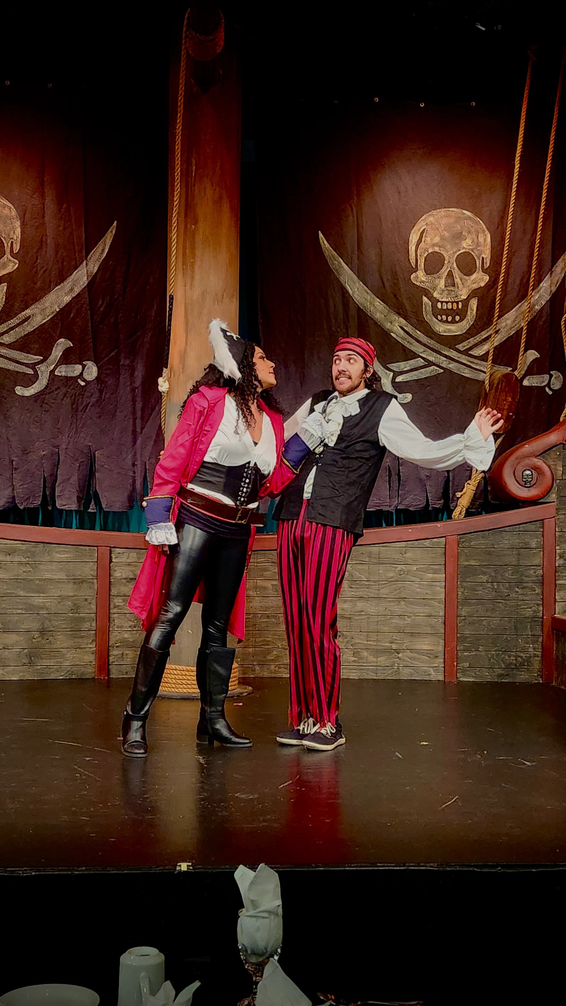 Two performers in pirate costumes act out a dramatic scene on a ship‑themed stage.