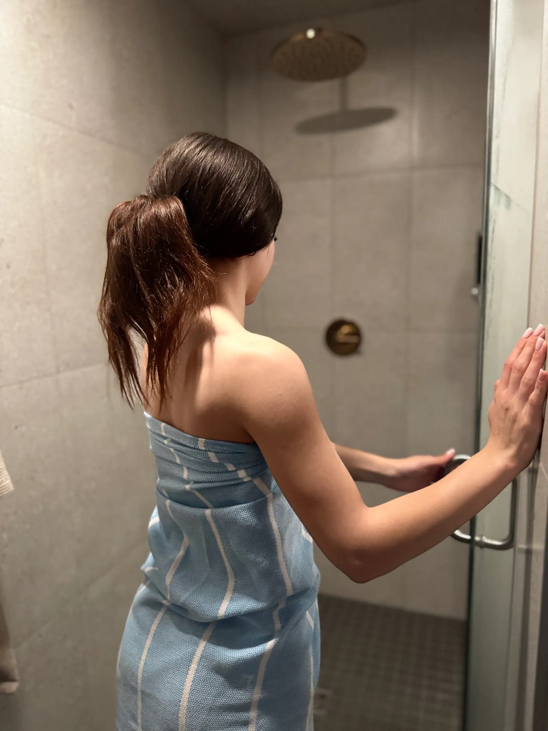 Person wrapped in a towel entering a softly lit spa shower room.