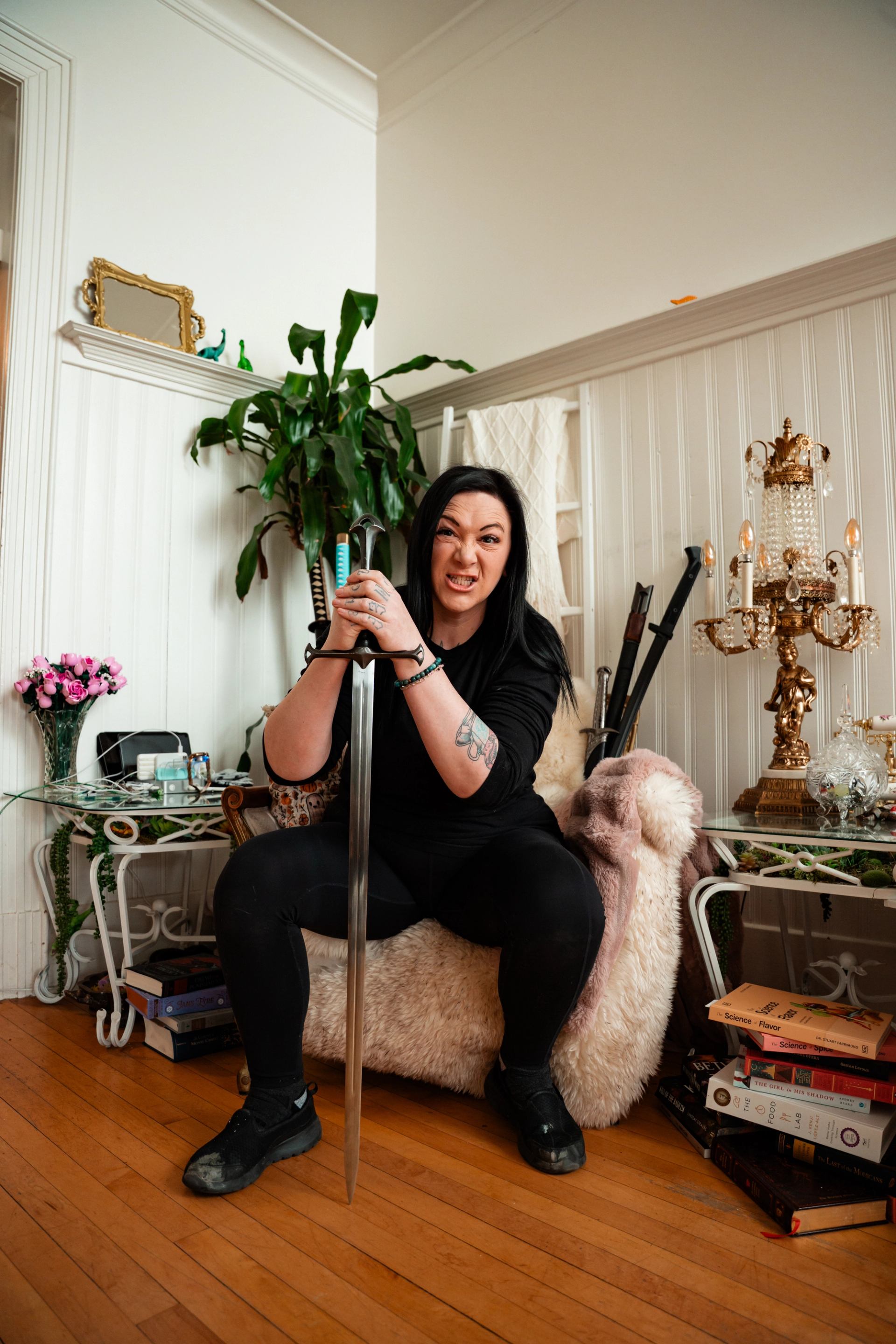Person in black clothing grips a long sword while sitting in an ornate living room.