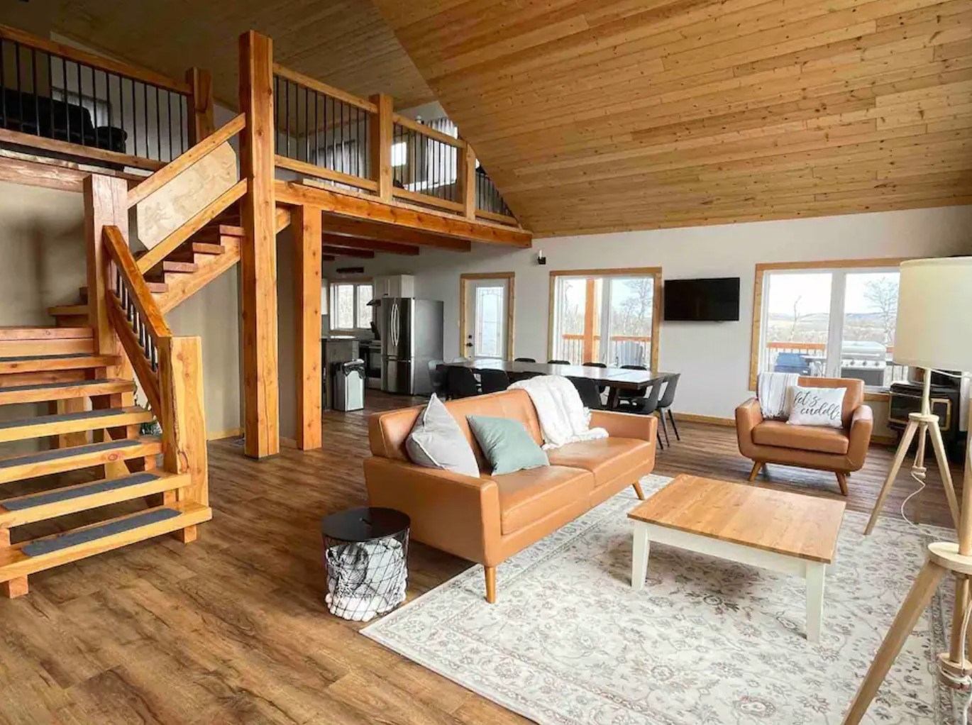 Cozy cabin living room with wood interior, loft stairs, and modern furniture.