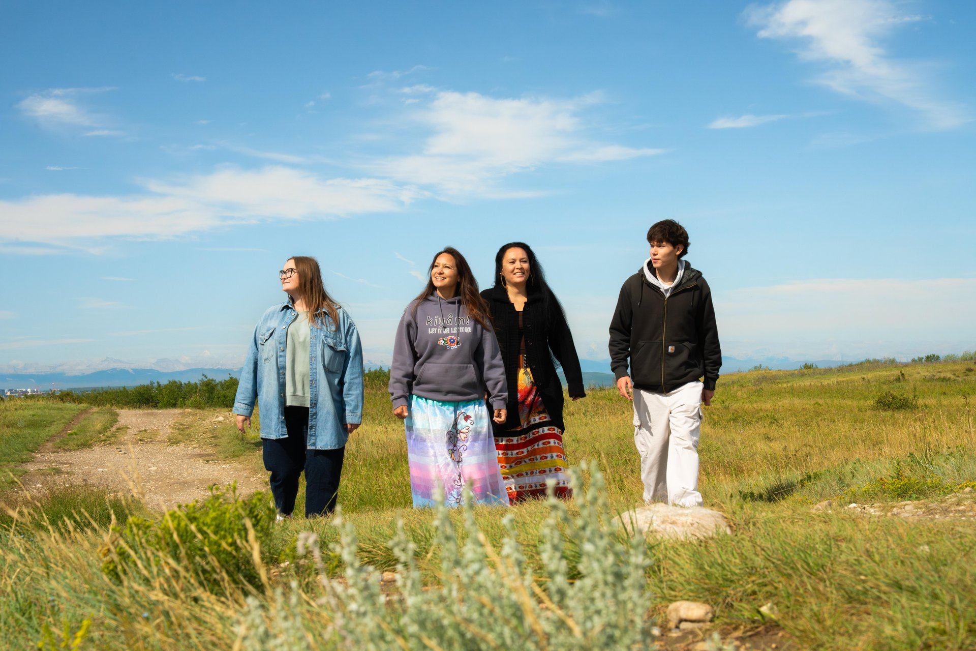 A small group walks together across open grassland under a bright blue sky.