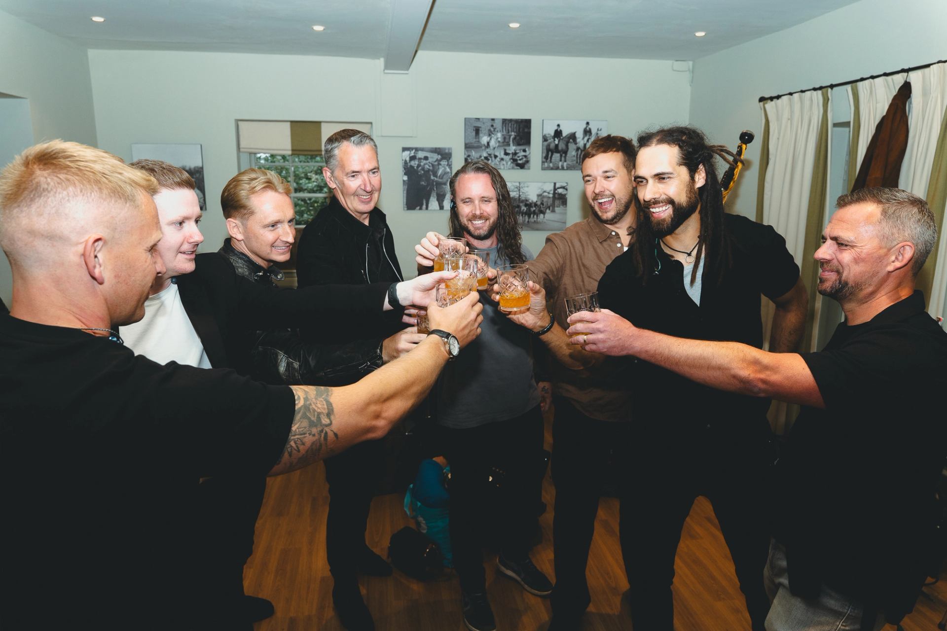 Group of people standing in a circle indoors, raising drinks in a toast.