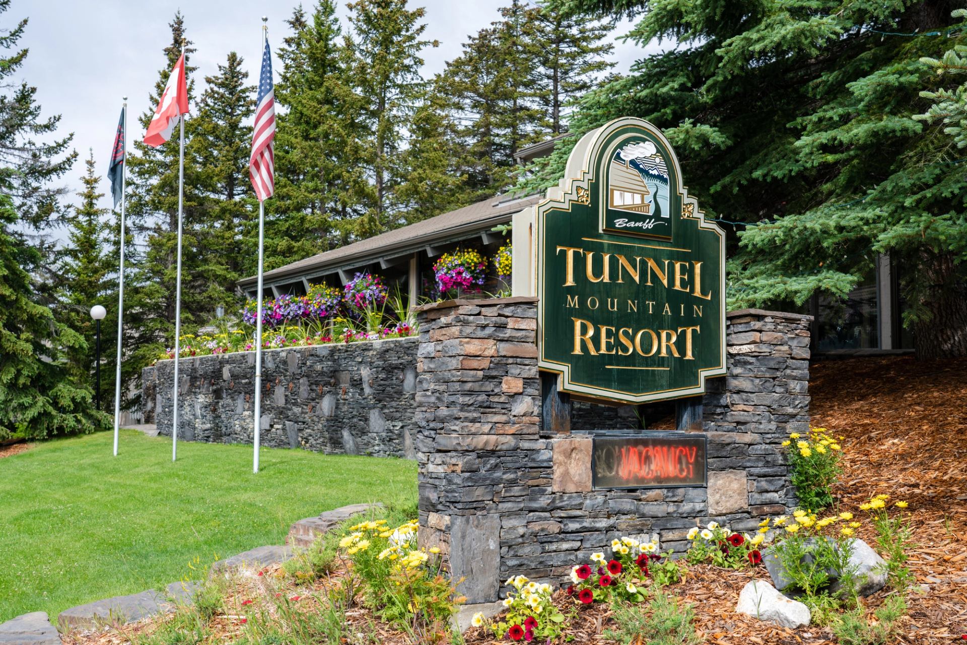Stone and wood resort sign with flowers, flags, and mountain-themed design.