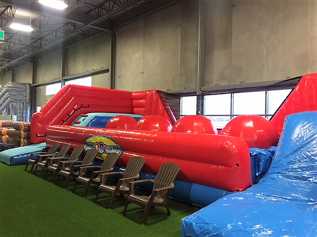 Indoor inflatable obstacle course with red and blue padded slides and plastic chairs.
