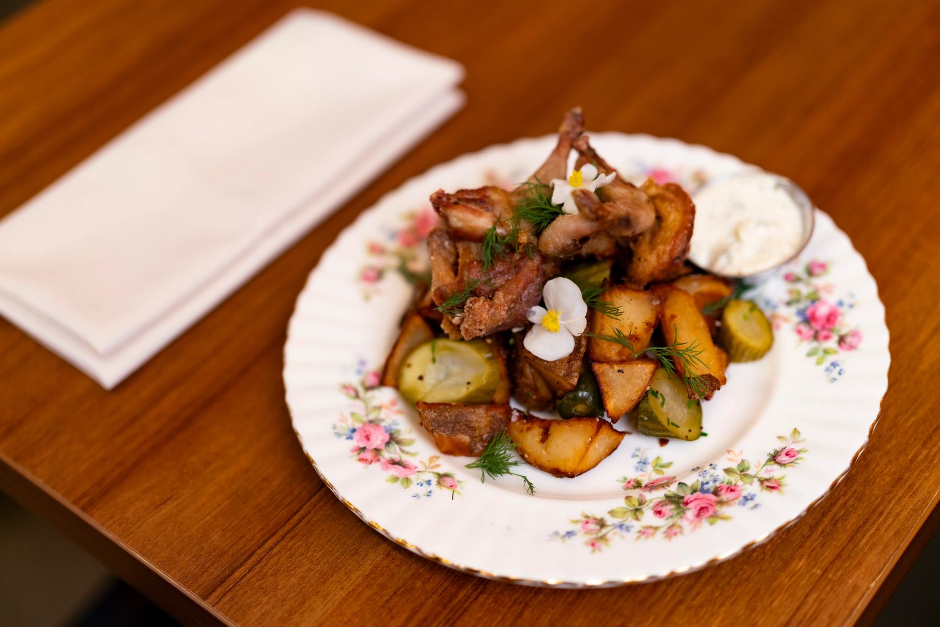 Roast chicken with potatoes, pickles and dill on floral plate beside folded napkin.