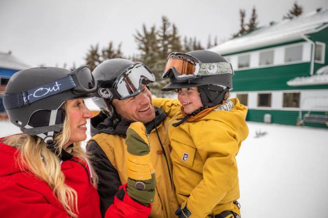 A young family, child in Dad's arms, chatting at the base of the hill before skiing at Hidden Valley Ski Resort.